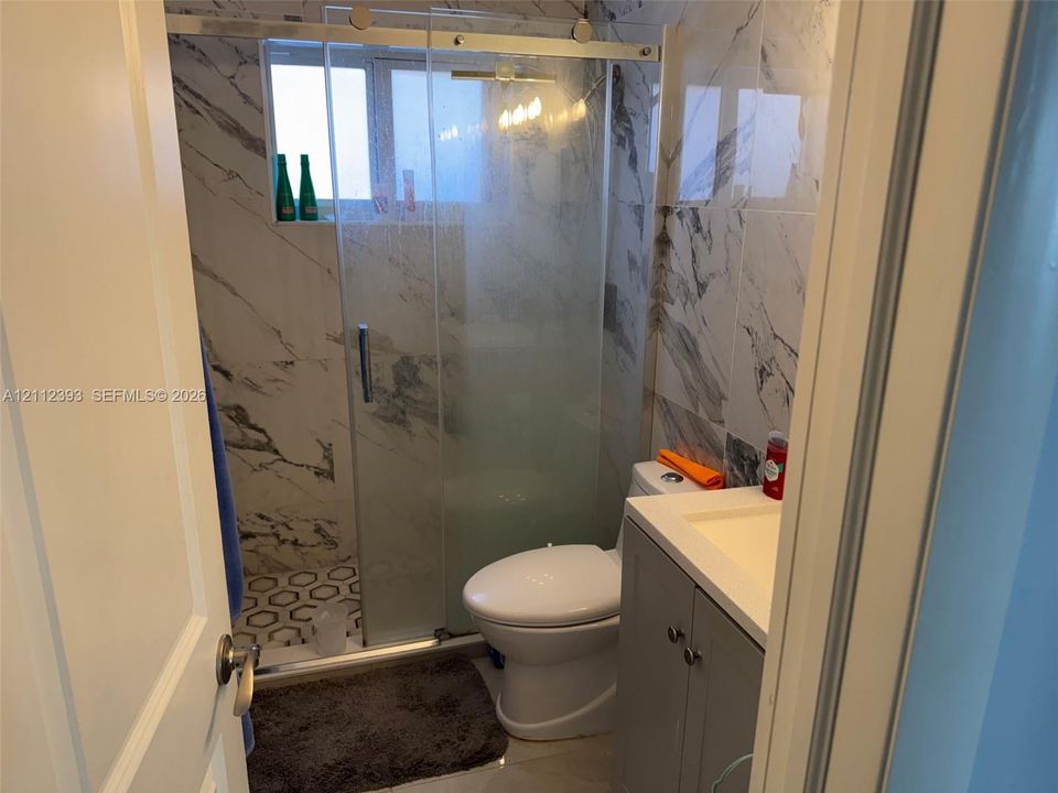 Bathroom featuring a glass-enclosed shower with sliding hardware, large-format marbled tile wall surrounds, decorative hexagon floor tile, and a grey vanity with an integrated countertop sink