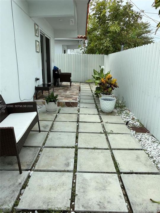 Concrete paver patio featuring white privacy fencing, multi-tone tile entry landing, and stone ground cover