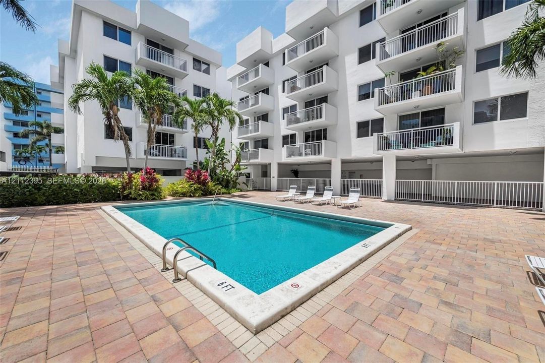 Outdoor swimming pool featuring a concrete deck and paver patio with perimeter fencing and tropical landscaping