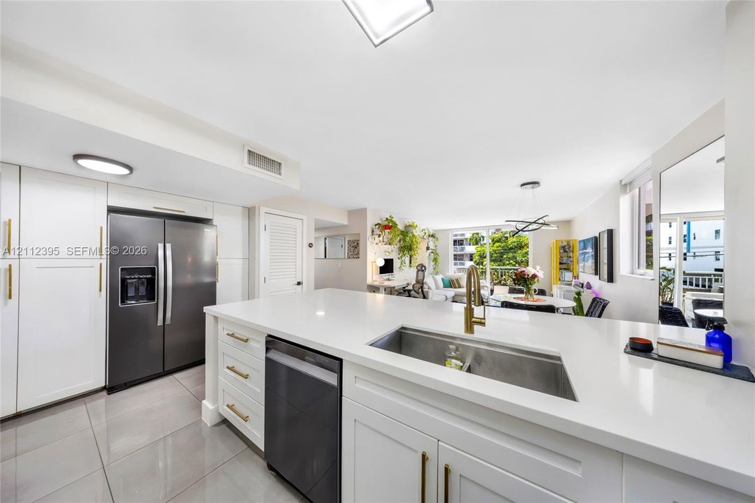 Kitchen featuring white cabinetry, quartz countertops, a stainless steel undermount sink with a brass-finish faucet, and stainless steel appliances