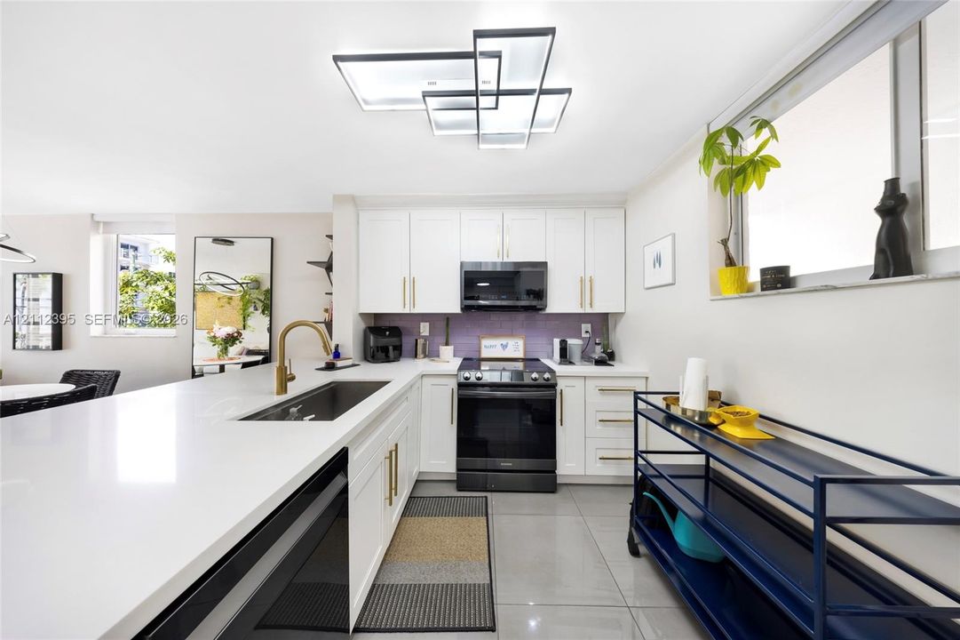 Kitchen featuring white cabinetry with brass hardware, expansive white countertops, a deep undermount sink with a brass faucet, large-format tile flooring, and a modern geometric LED ceiling fixture