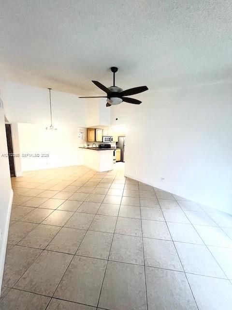Large-format tile flooring, vaulted ceilings, and a ceiling fan with integrated lighting