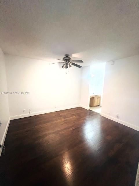Interior space featuring dark wood-finish flooring, neutral wall tones, and a ceiling fan with integrated multi-bulb lighting fixture