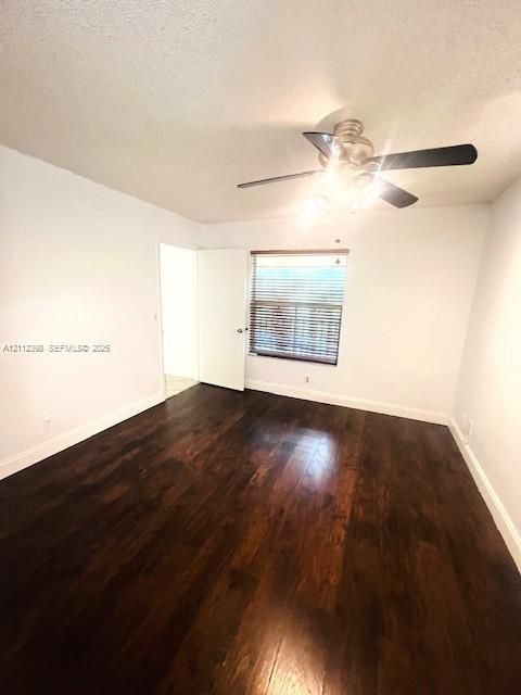 Interior room featuring dark wood-finish flooring, a ceiling fan with integrated lighting, and horizontal window blinds