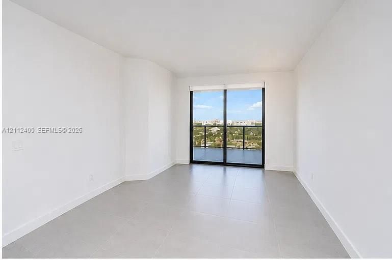 Interior space featuring large-format ceramic tile flooring, neutral wall finishes, and floor-to-ceiling glass sliding doors opening to a balcony with a black metal railing