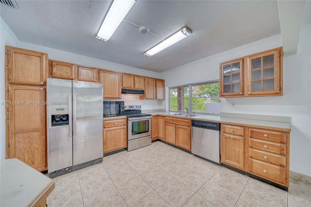 Kitchen featuring medium-tone wood cabinetry, solid-surface countertops, tile flooring, and a stainless steel appliance package including a refrigerator, dishwasher, and electric range