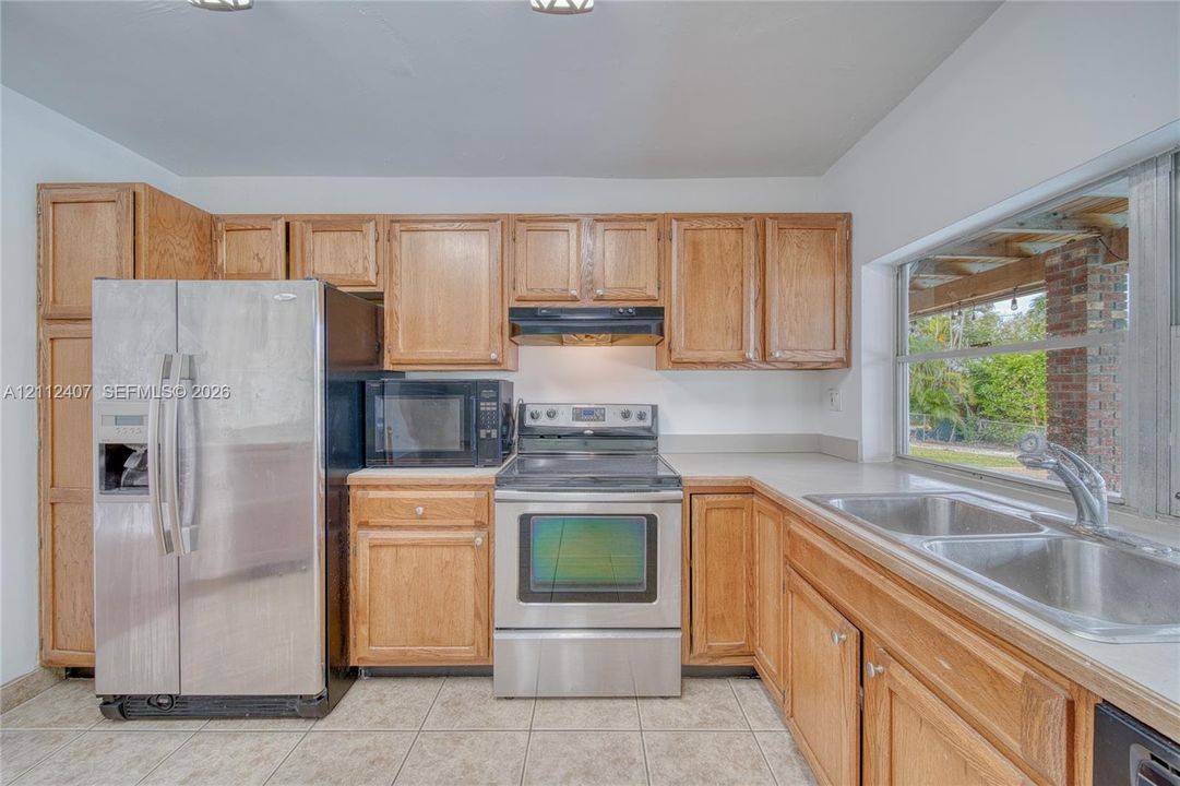 Kitchen featuring oak-finish cabinetry, stainless steel appliances, a double-basin stainless steel sink, and ceramic tile flooring