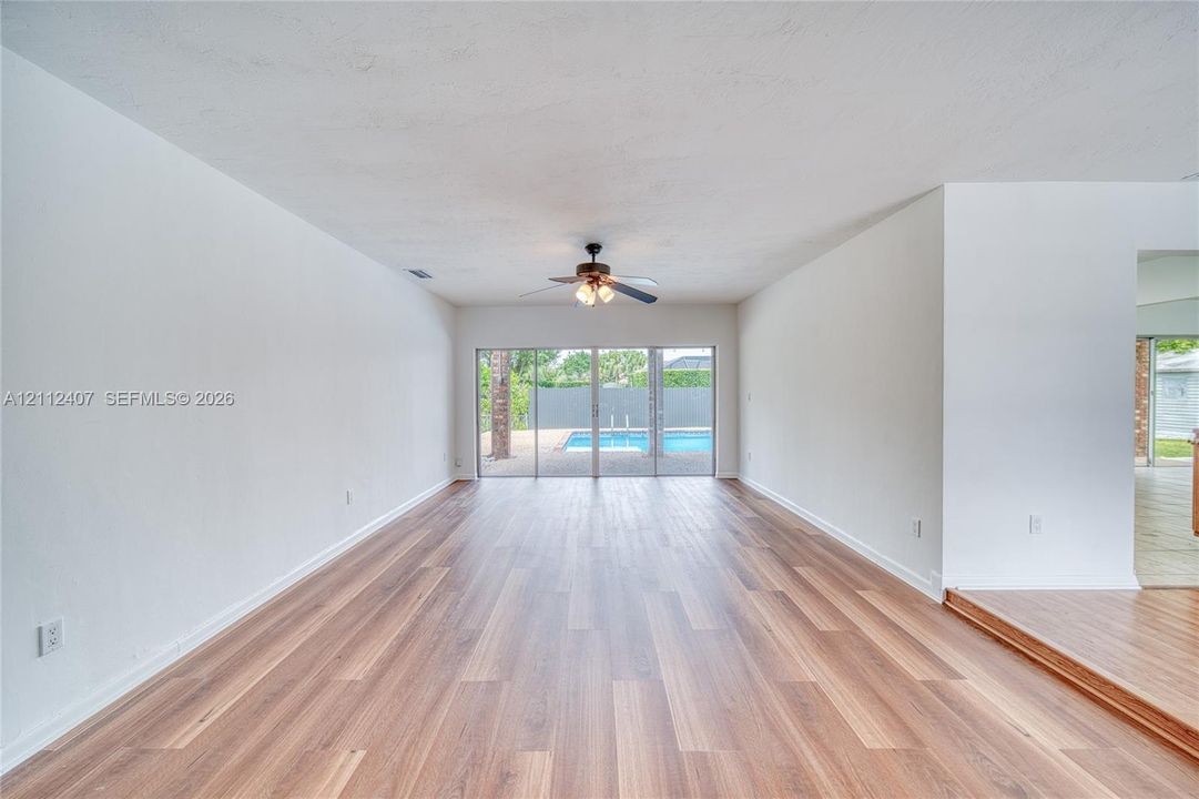 Interior living space featuring wood-finish flooring, a ceiling fan with integrated lighting, and glass sliding doors revealing a swimming pool