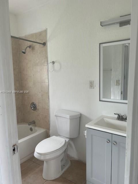 Bathroom featuring a gray vanity with an integrated sink, a rectangular framed mirror, a tub-shower combination with neutral-toned tiled surround, and a wall-mounted light fixture