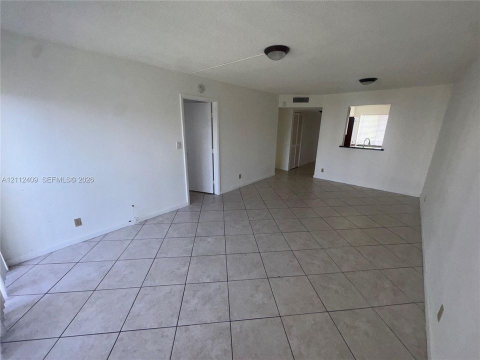 Open-concept interior featuring neutral tile flooring, flush-mount ceiling lighting, and a kitchen passthrough window