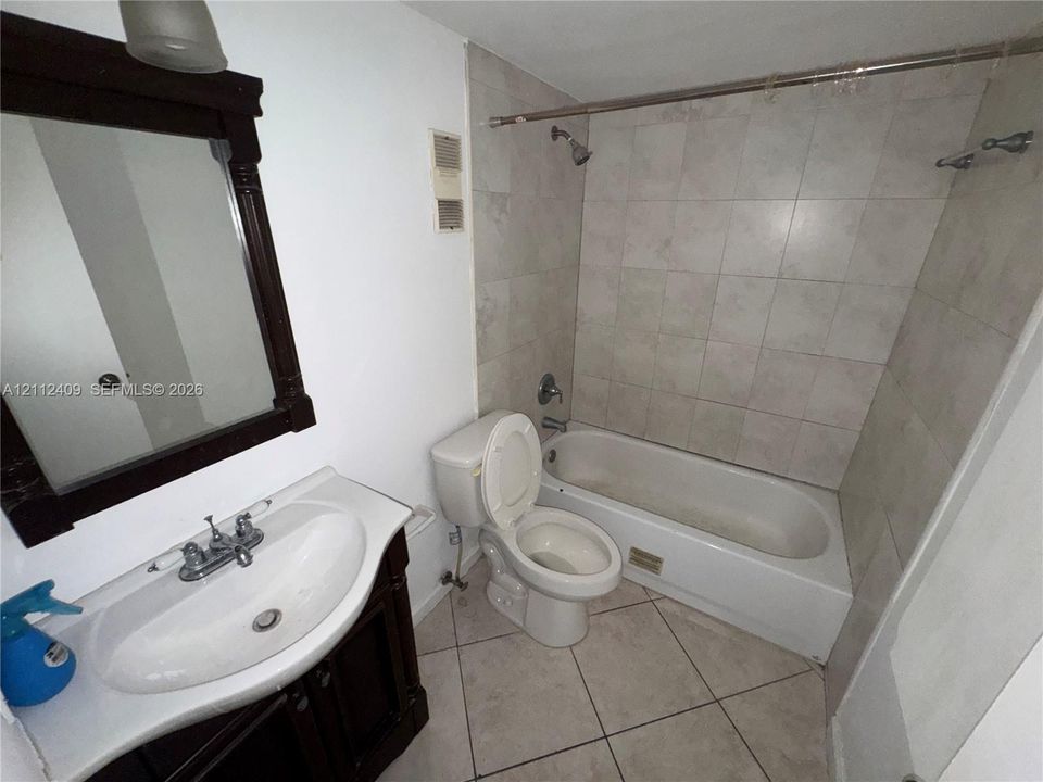 Bathroom featuring tile flooring, a dark-finish wood vanity, a wall-mounted mirror with a matching frame, and a tub-shower combination enclosed by neutral-toned wall tile