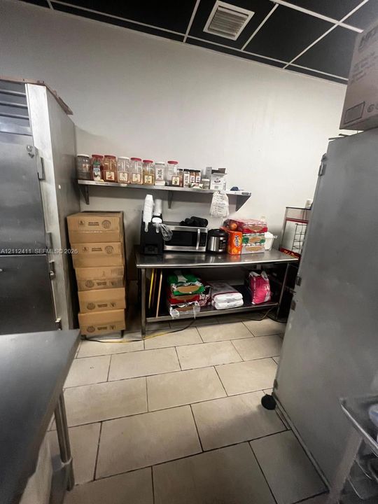 Commercial kitchen space featuring stainless steel prep tables, large-format tile flooring, and wall-mounted metal shelving