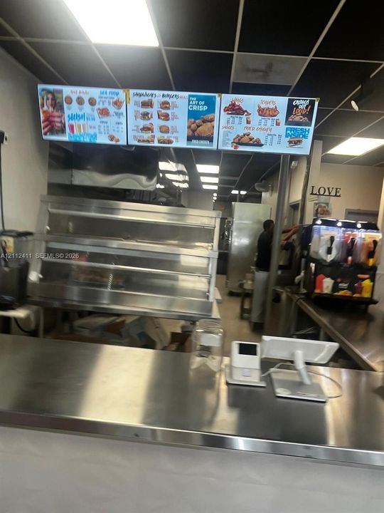 Commercial food service area featuring stainless steel preparation counters, integrated stainless steel shelving, and a drop-ceiling with recessed lighting