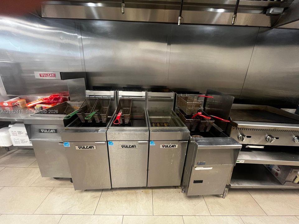 Commercial kitchen featuring multiple stainless steel Vulcan deep fryers, a flat-top grill, and a stainless steel wall-mounted ventilation hood