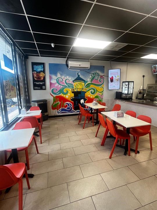 Interior space featuring large-format ceramic tile flooring, a grid-pattern drop ceiling, floor-to-ceiling windows, wall-mounted air conditioning unit, and a painted mural