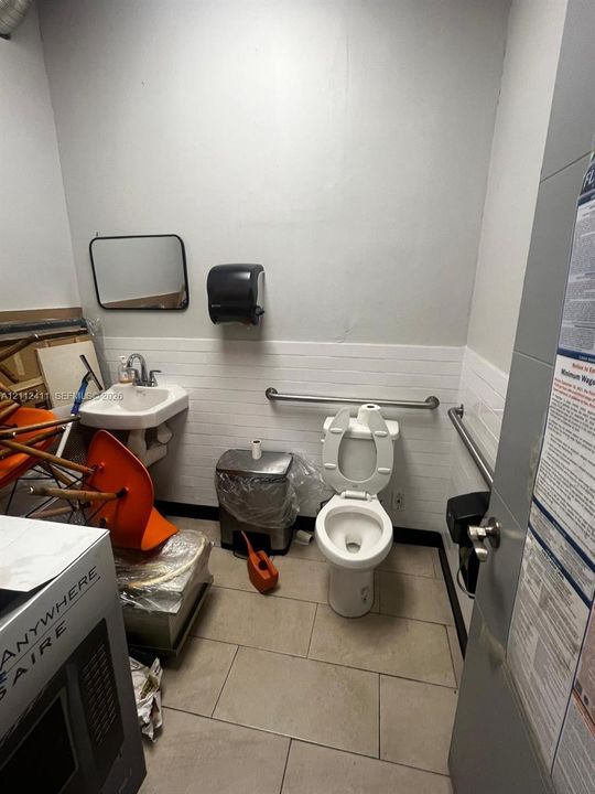 Restroom featuring ceramic tile flooring, wall-mounted porcelain sink, subway tile wainscoting, and stainless steel grab bars