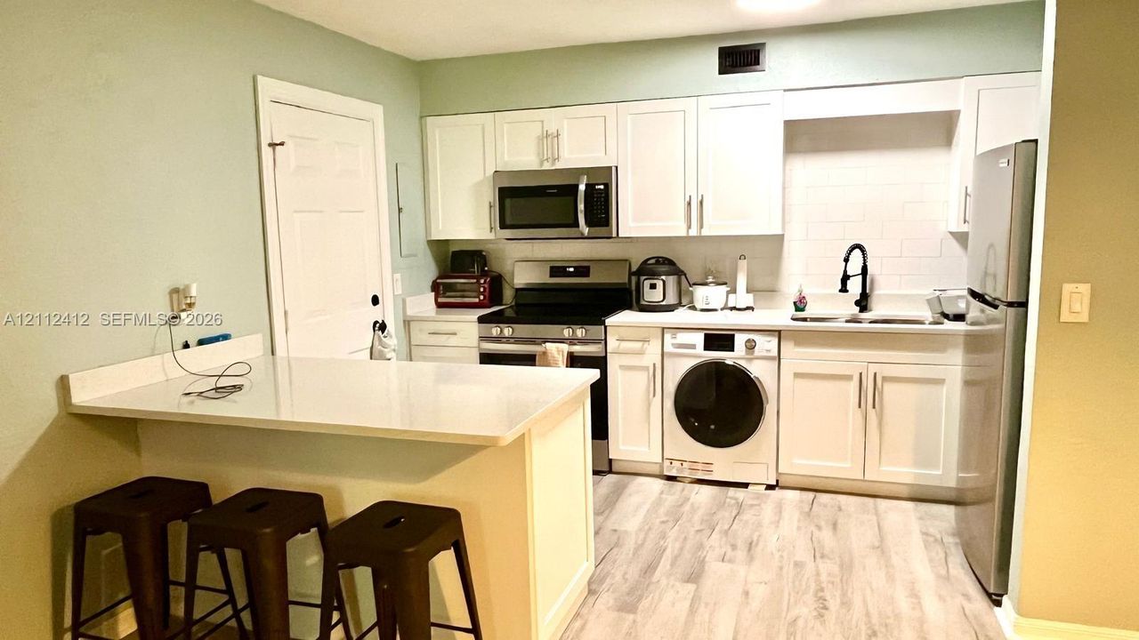 Kitchen featuring white cabinetry, wood-finish flooring, a quartz countertop peninsula, stainless steel appliances, and a matte black faucet