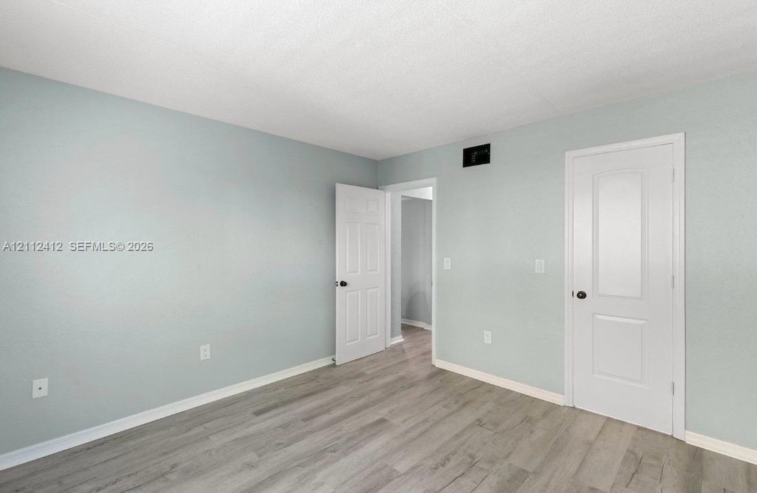 Room featuring neutral-toned walls, wood-finish flooring, and white two-panel interior doors with matte black hardware