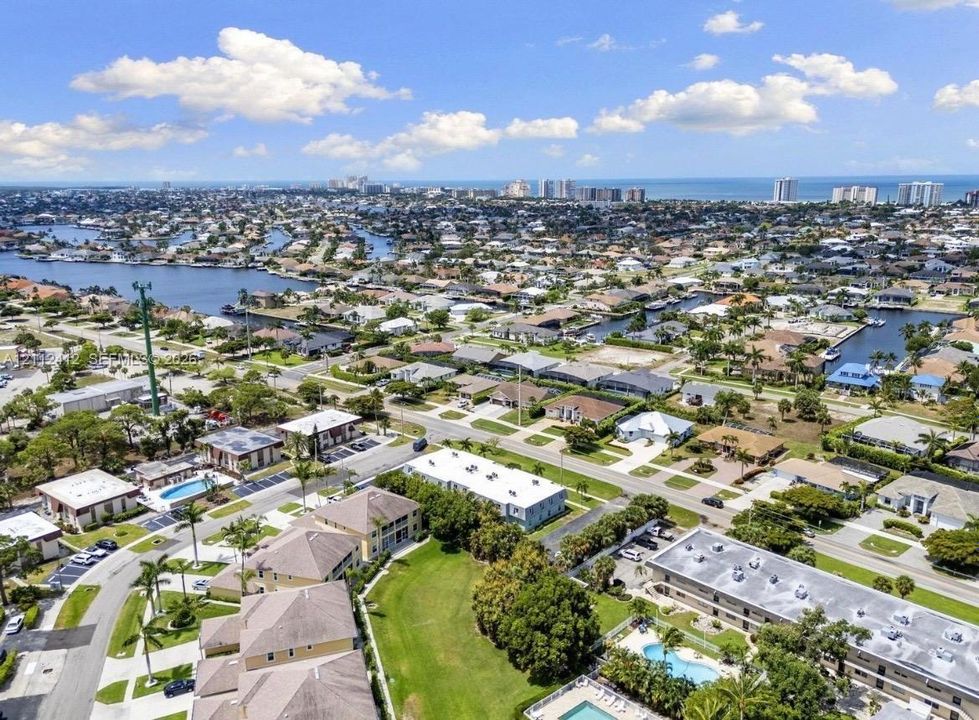 Aerial perspective of coastal residential area featuring waterfront canals, mature landscaping, community swimming pools, and proximity to the ocean