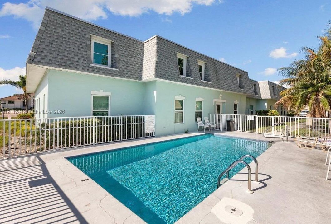 In-ground swimming pool featuring a concrete deck and metal perimeter fencing, accompanied by a multi-level structure with a mansard roof and exterior stucco finish
