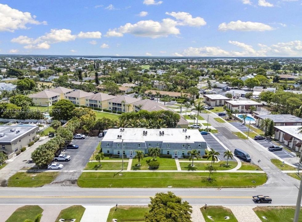 Aerial perspective of a multi-unit complex featuring a low-rise exterior, dedicated asphalt parking area, concrete walkways, and manicured lawn landscaping