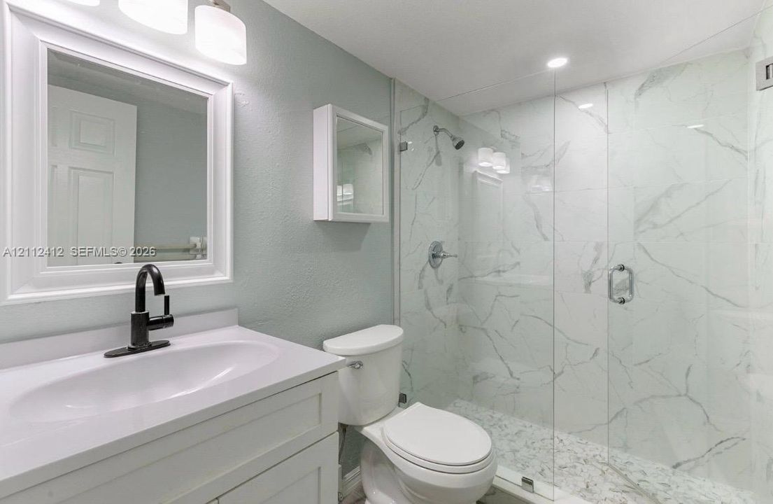 Bathroom featuring a white vanity cabinet, matte black faucet, wall-mounted medicine cabinet, and a walk-in shower with floor-to-ceiling stone-patterned tile and a frameless glass door