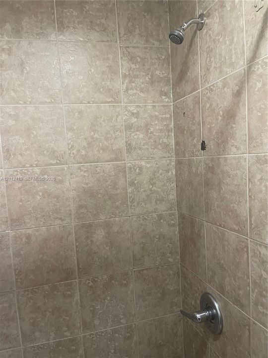 Shower enclosure featuring neutral-toned wall tiles, a metallic single-handle pressure balance valve, and a wall-mounted shower head