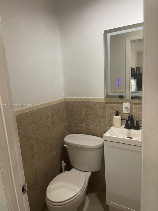 Wall-mounted LED backlit mirror, pedestal-style vanity with a rectangular sink, matte black faucet, and tiled wainscoting
