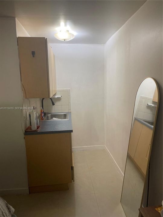 Compact kitchenette featuring light-finish cabinetry, a neutral solid-surface countertop, stainless steel drop-in sink, tile backsplash, and ceramic floor tiling