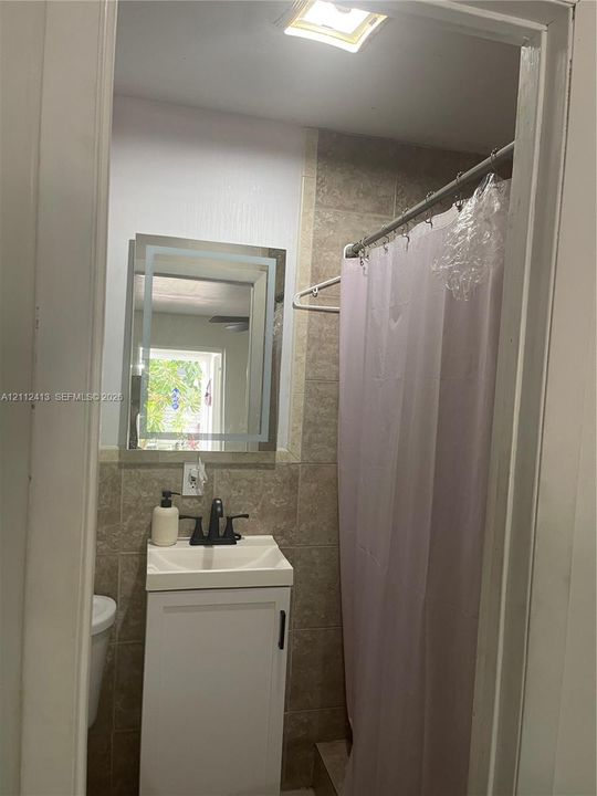 Bathroom featuring a vanity with a white basin, matte black faucet, illuminated wall mirror, and tile-surround shower area