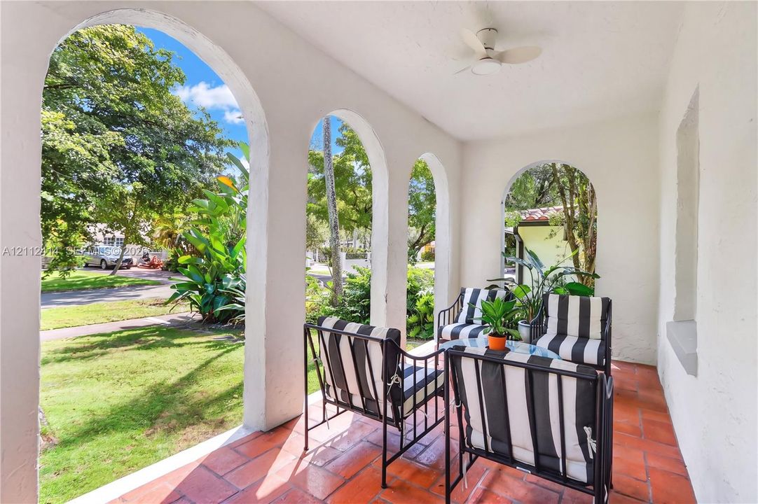 Covered porch featuring arched masonry openings, clay tile flooring, and a ceiling-mounted fan
