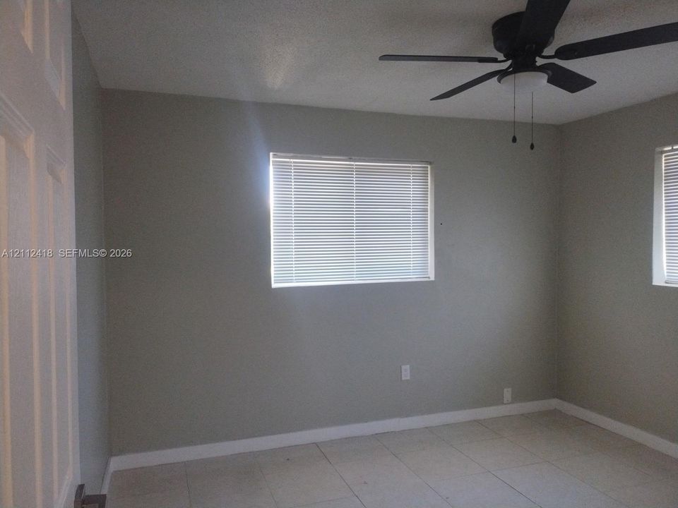 Neutral-toned walls featuring tile flooring, horizontal window blinds, and a multi-blade ceiling fan with integrated lighting