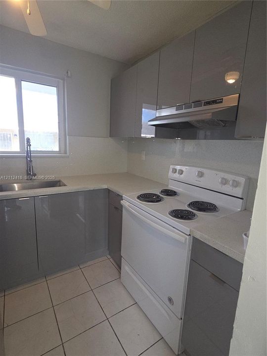 Kitchen featuring high-gloss grey cabinetry, stone-finish countertops, stainless steel undermount sink with a gooseneck faucet, white electric range, and tile flooring