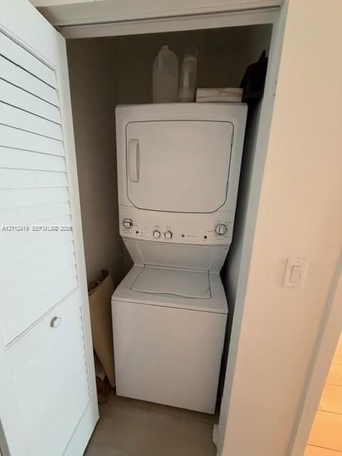 Laundry closet featuring a white stacked washer and dryer unit concealed behind a louvered bi-fold door