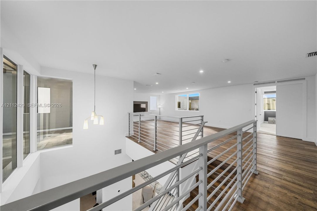Open-concept interior featuring wood-finish flooring, a multi-light pendant fixture, horizontal metal railing system, and recessed lighting