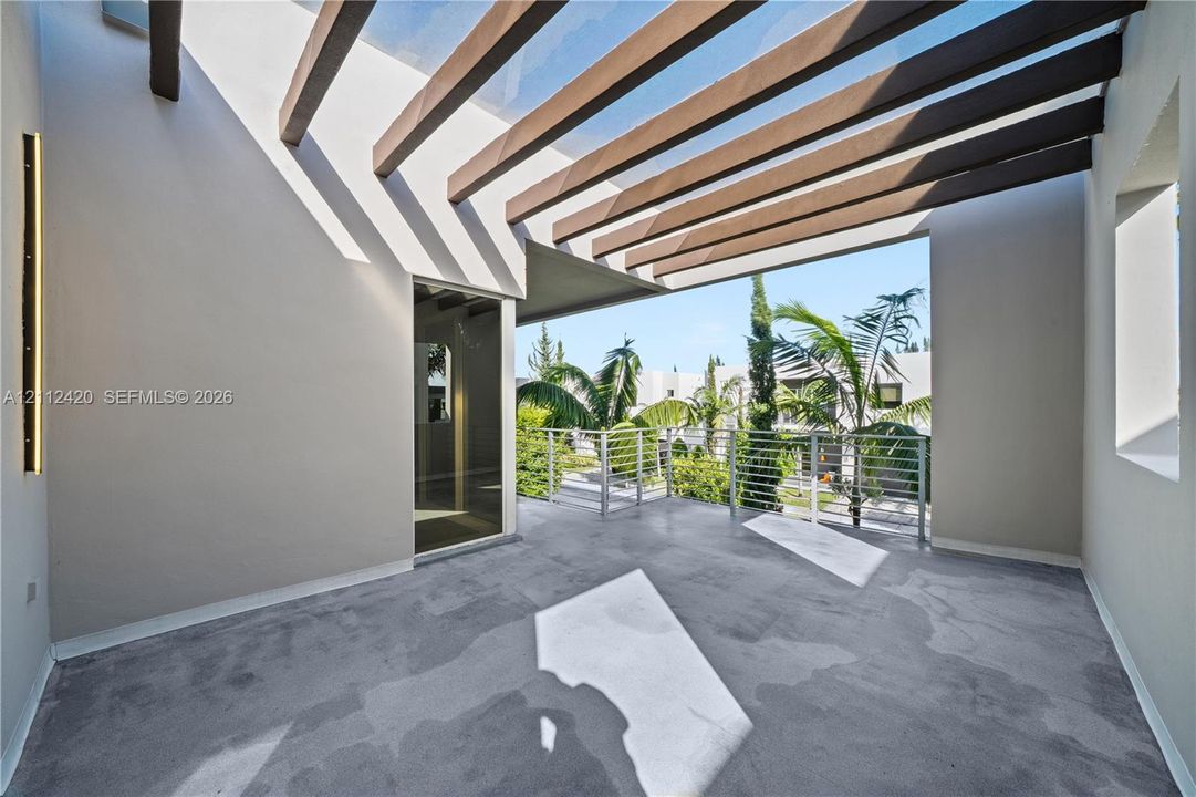Covered balcony featuring a wood-beam pergola, concrete flooring, vertical accent lighting, and a metal railing