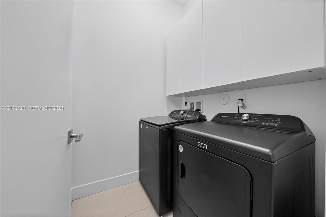 Dedicated laundry area featuring white wall-mounted cabinetry and light-toned tile flooring