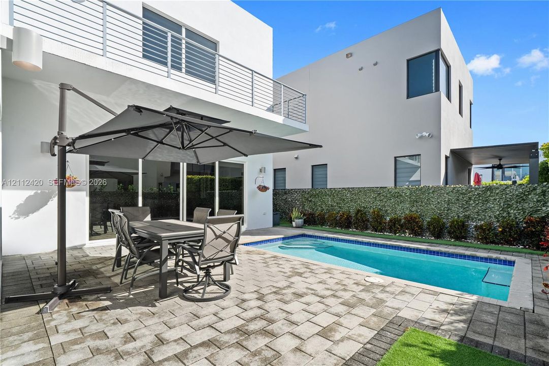 Modern exterior featuring a paved stone patio, in-ground swimming pool, horizontal metal balcony railing, and floor-to-ceiling sliding glass doors