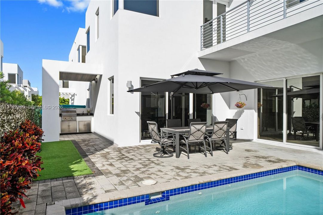 Modern exterior with a swimming pool, stone-paver patio, built-in outdoor kitchen, and a second-story balcony featuring metal railing