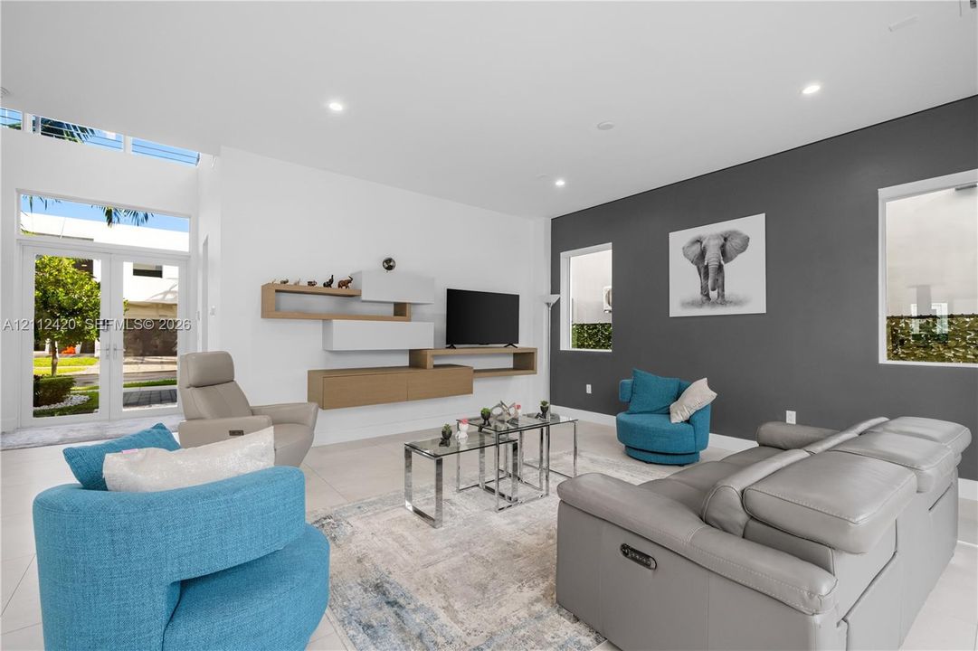 Living area featuring high ceilings, large-format tile flooring, a custom wall-mounted storage unit, recessed lighting, and an accent wall with windows