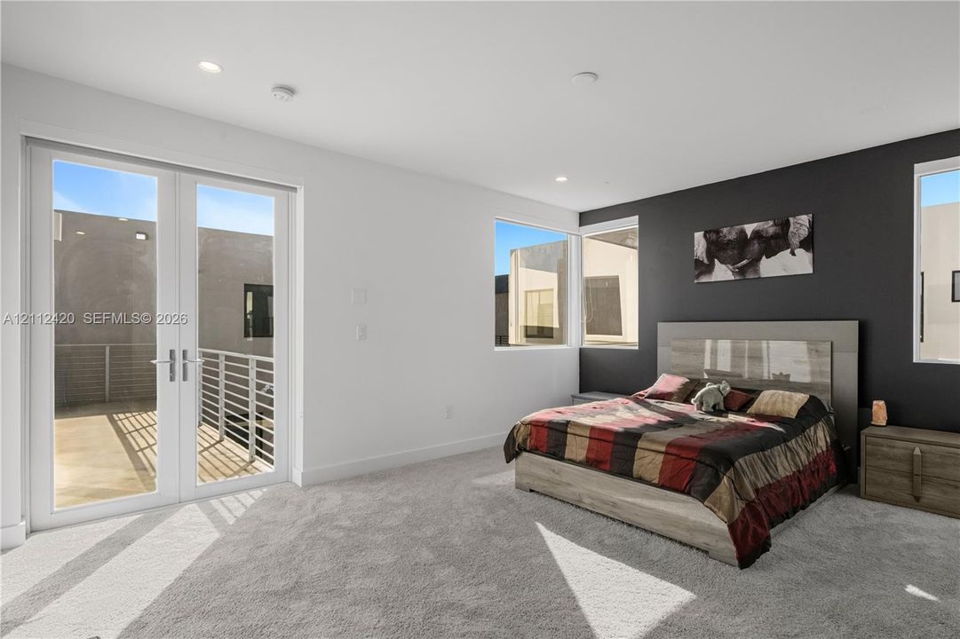 Interior space featuring recessed lighting, carpeted flooring, a dark accent wall, and double-glass doors opening to an exterior balcony with a metal railing
