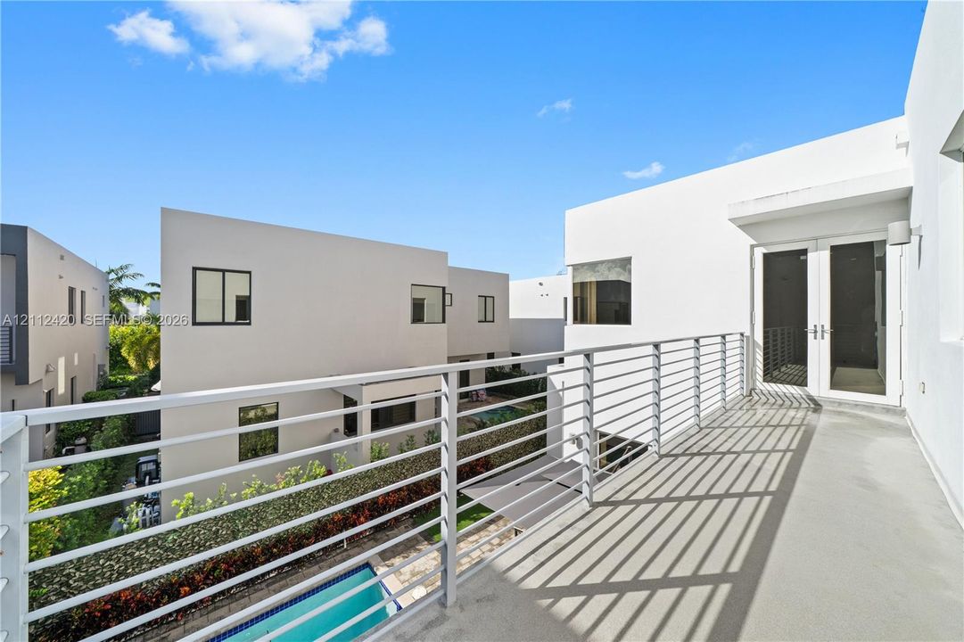 Modern balcony featuring sleek metal railing, smooth concrete flooring, and double-glass entry doors