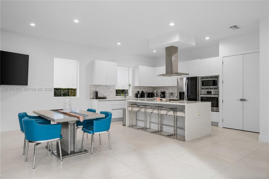 Kitchen featuring flat-panel cabinetry, a quartz-topped center island with integrated seating, stainless steel appliances, a chimney-style range hood, and tile flooring