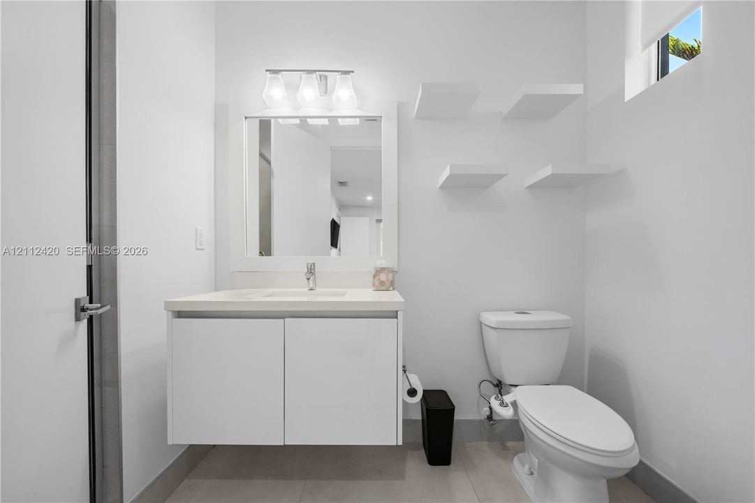 Modern floating vanity with a solid-surface countertop and integrated sink, complemented by built-in wall shelving, a rectangular mirror, and a three-light fixture