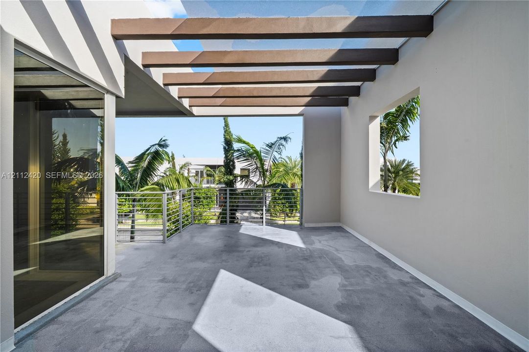 Covered balcony featuring exposed wooden ceiling beams, concrete flooring, and metal horizontal railings
