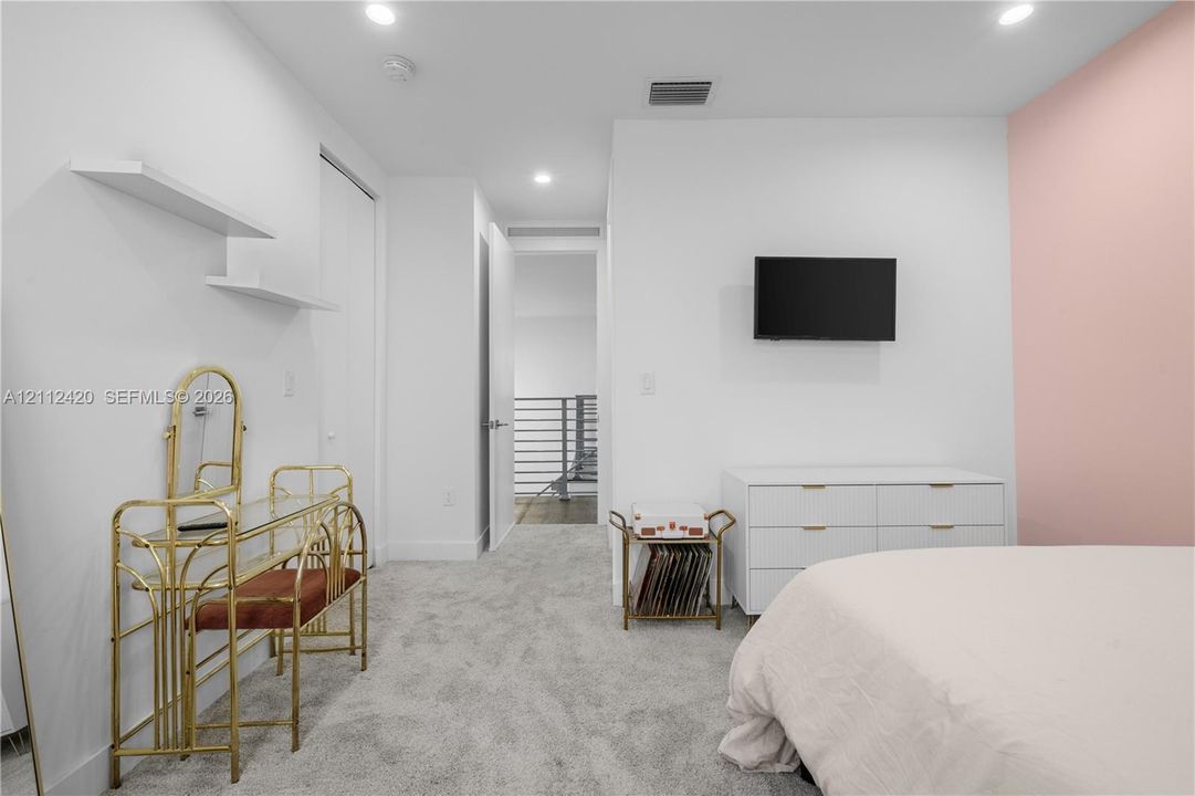 Neutral interior featuring wall-to-wall carpeting, recessed ceiling lighting, dual floating wall shelves, and a single-wall accent color