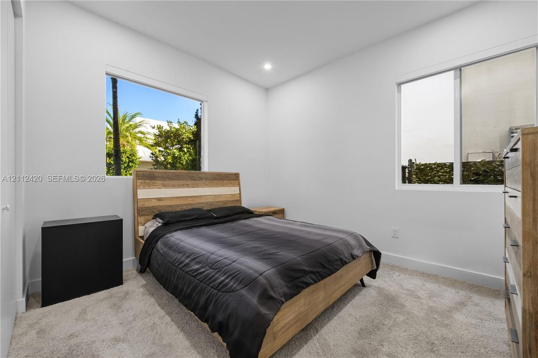 Neutral interior space featuring high-pile carpeting, smooth-finish walls, recessed ceiling lighting, and dual windows with exterior palm tree exposure