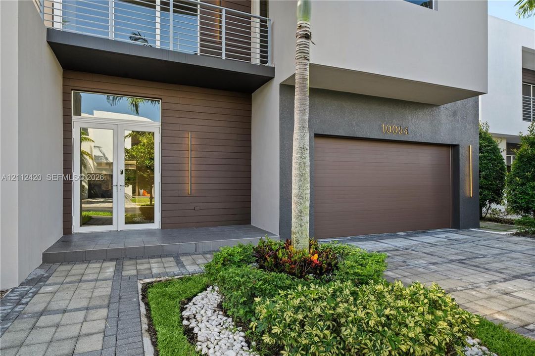 Contemporary exterior featuring a horizontal wood-plank facade, second-story balcony with metal railing, double-door entryway, and paver driveway