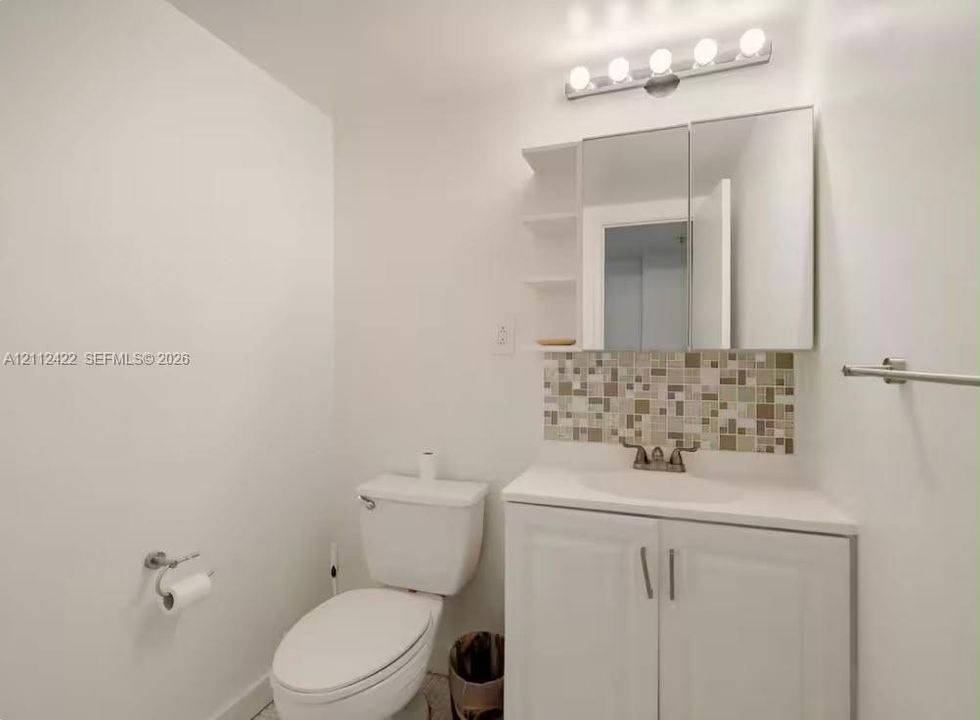 White vanity with integrated basin, multicolor mosaic tile backsplash, mirrored medicine cabinet with integrated shelving, and five-bulb vanity light fixture