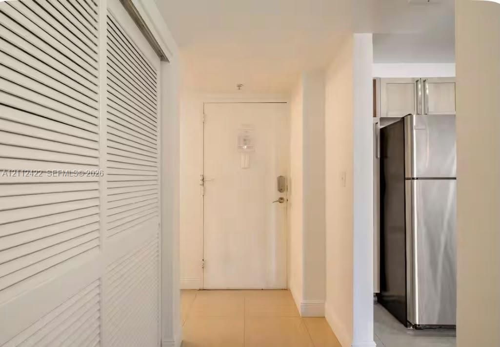 Entryway featuring dual louvered-door closets, neutral tile flooring, and a stainless steel refrigerator